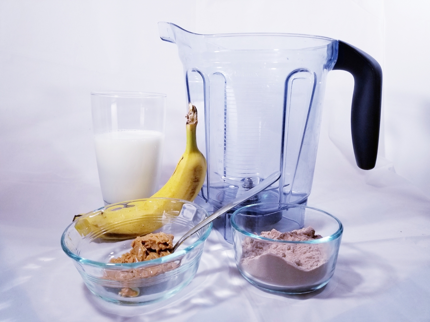 picture of the ingredients used in this recipe. Milk, a banana, peanut butter, protein powder, and the blender container.